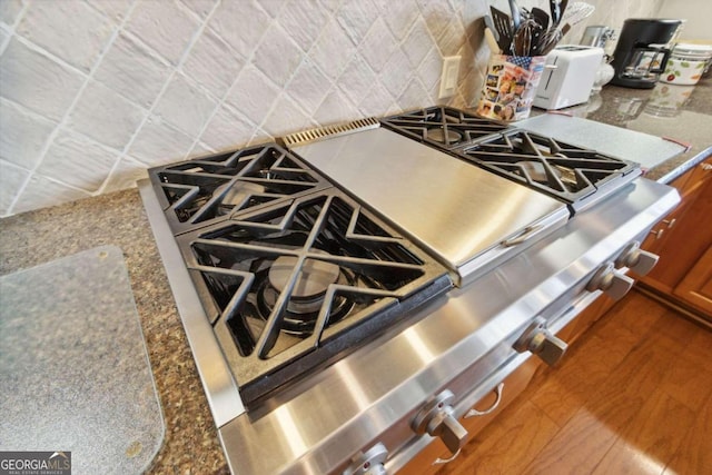 interior details featuring stone countertops, gas range oven, decorative backsplash, and hardwood / wood-style floors