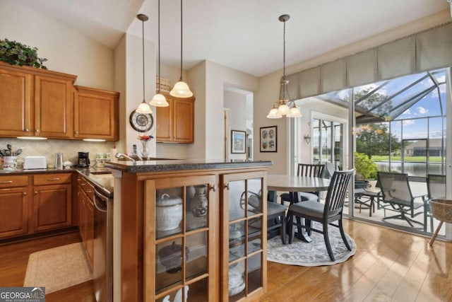 kitchen with lofted ceiling, backsplash, stainless steel dishwasher, light hardwood / wood-style floors, and decorative light fixtures