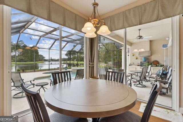 dining area with ceiling fan with notable chandelier, wood-type flooring, a water view, and plenty of natural light