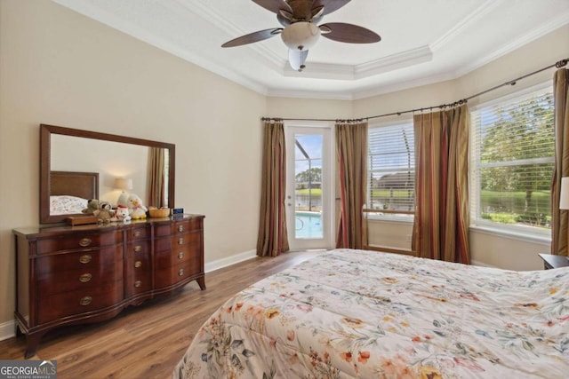 bedroom with multiple windows, light wood-type flooring, ceiling fan, and a raised ceiling