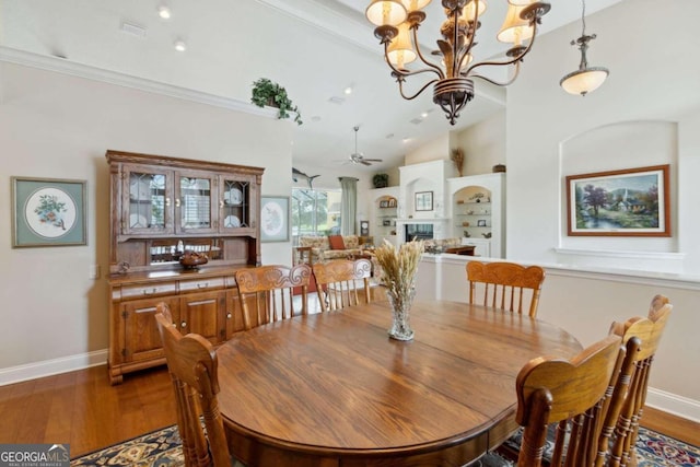 dining area with hardwood / wood-style flooring, built in shelves, ceiling fan with notable chandelier, crown molding, and vaulted ceiling