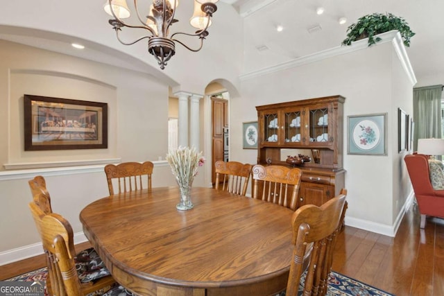 dining room featuring wood-type flooring, a notable chandelier, crown molding, and decorative columns