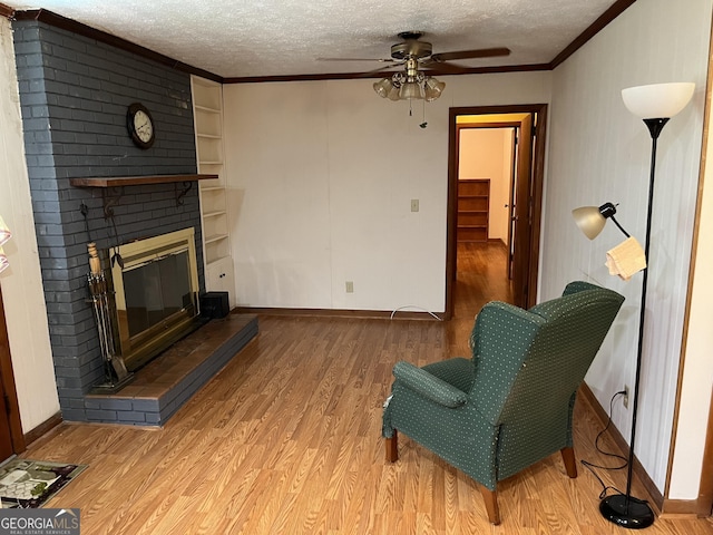 sitting room with a brick fireplace, a textured ceiling, ornamental molding, ceiling fan, and light hardwood / wood-style floors