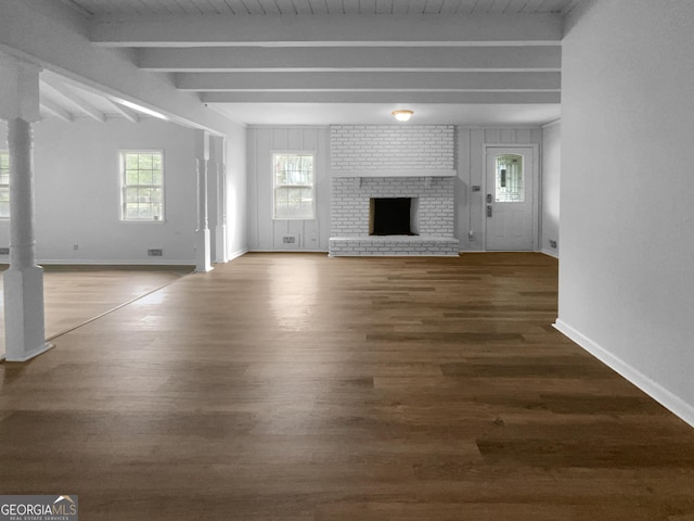 unfurnished living room featuring a brick fireplace, beam ceiling, and dark hardwood / wood-style floors