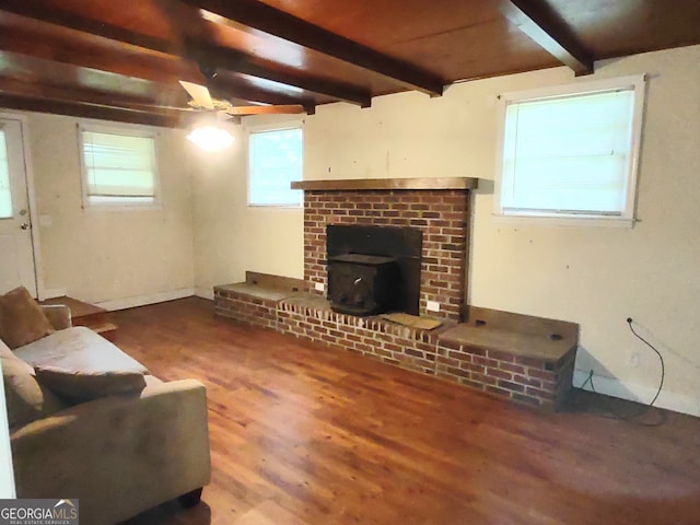 living room featuring beam ceiling, hardwood / wood-style floors, a wood stove, ceiling fan, and a brick fireplace