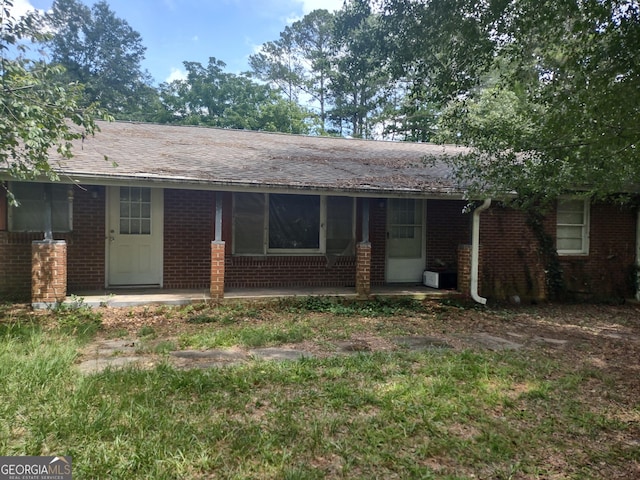 back of property featuring covered porch, a shingled roof, and brick siding