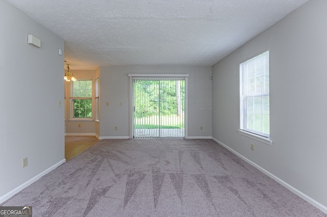 carpeted empty room with an inviting chandelier and a textured ceiling