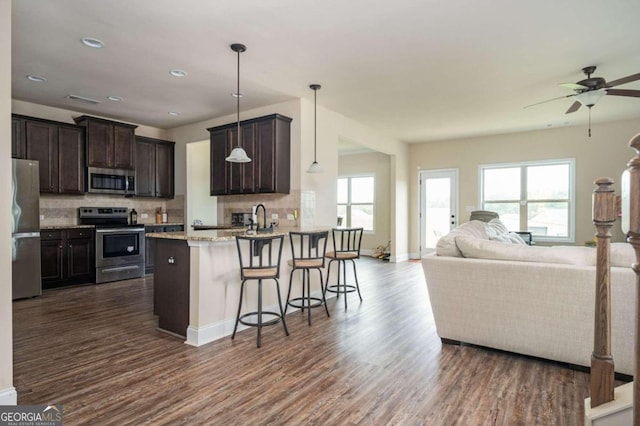 kitchen featuring decorative backsplash, dark hardwood / wood-style floors, hanging light fixtures, stainless steel appliances, and a breakfast bar