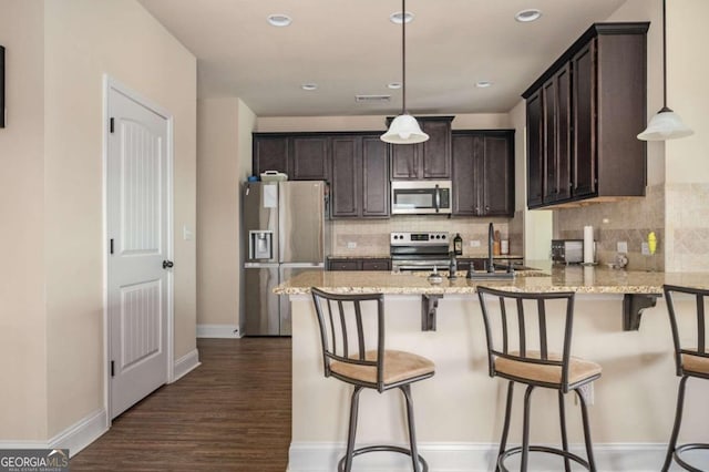 kitchen featuring pendant lighting, light stone countertops, stainless steel appliances, and dark hardwood / wood-style flooring