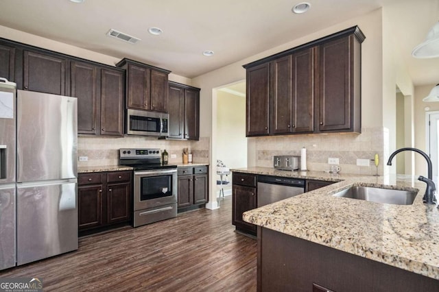 kitchen with decorative backsplash, dark wood-type flooring, dark brown cabinets, sink, and appliances with stainless steel finishes