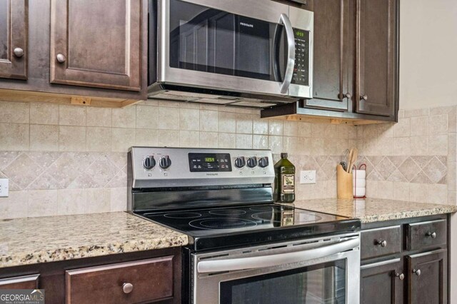 kitchen with dark brown cabinets, light stone counters, stainless steel appliances, and backsplash