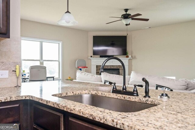 kitchen featuring dark brown cabinets, backsplash, ceiling fan, a tile fireplace, and sink