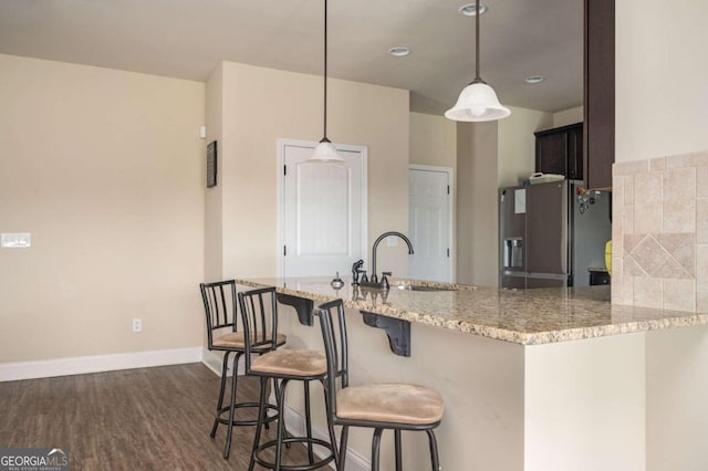 kitchen featuring a kitchen bar, dark hardwood / wood-style flooring, kitchen peninsula, hanging light fixtures, and stainless steel fridge