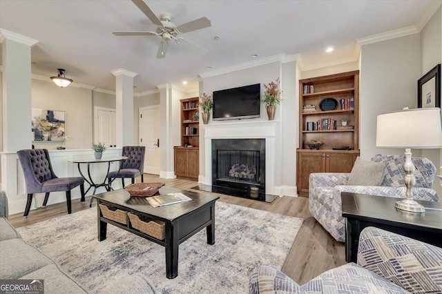 living room featuring ceiling fan, light hardwood / wood-style flooring, crown molding, and ornate columns