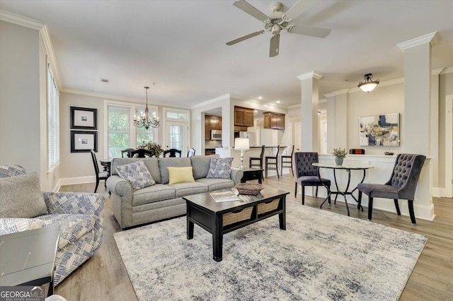 living room featuring decorative columns, ceiling fan with notable chandelier, crown molding, and light hardwood / wood-style floors