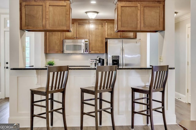 kitchen featuring a breakfast bar, appliances with stainless steel finishes, ornamental molding, and light wood-type flooring