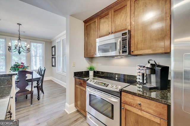 kitchen featuring dark stone countertops, hanging light fixtures, appliances with stainless steel finishes, light wood-type flooring, and ornamental molding