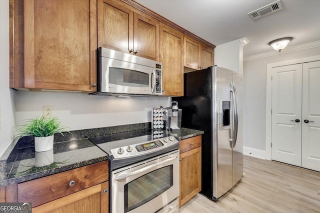 kitchen with ornamental molding, light hardwood / wood-style floors, dark stone countertops, and appliances with stainless steel finishes