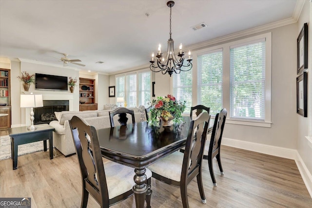 dining space with built in features, light wood-type flooring, ceiling fan with notable chandelier, and ornamental molding