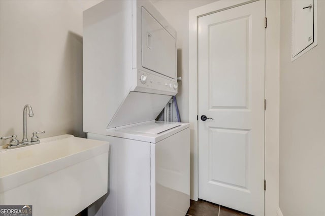 laundry area with sink, dark tile patterned floors, and stacked washer and dryer