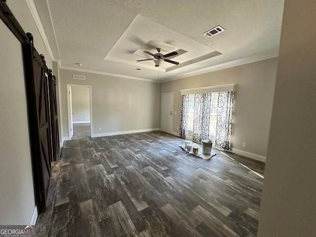 empty room with dark wood-type flooring, ceiling fan, a raised ceiling, and a barn door