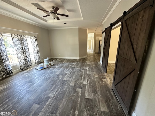 empty room with a barn door, a tray ceiling, ceiling fan, ornamental molding, and dark hardwood / wood-style floors