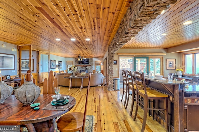 dining area featuring wood ceiling, a stone fireplace, ceiling fan, and light wood-type flooring