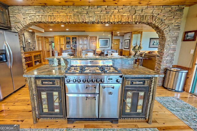 kitchen with dark stone counters, stainless steel appliances, dark brown cabinets, light hardwood / wood-style floors, and wooden ceiling