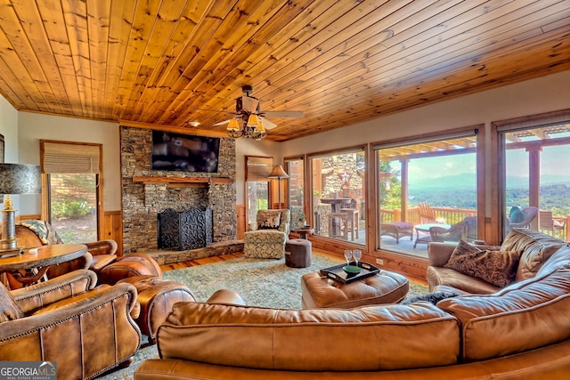 living room with hardwood / wood-style flooring, ceiling fan, a stone fireplace, and wooden ceiling