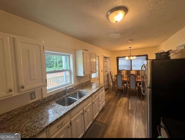 kitchen featuring a notable chandelier, dark wood-type flooring, pendant lighting, stainless steel fridge, and sink