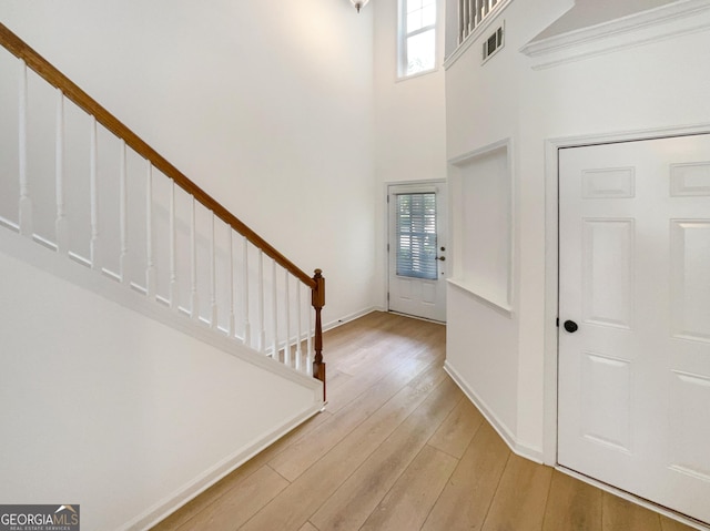 entryway with light hardwood / wood-style floors, a towering ceiling, a wealth of natural light, and ornamental molding