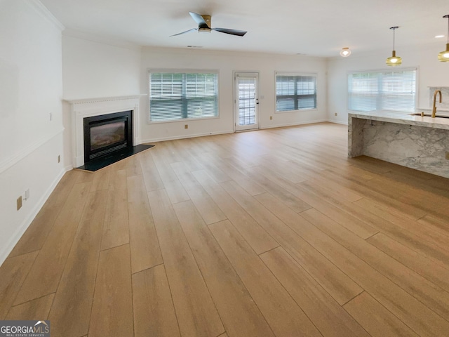 unfurnished living room featuring sink, ceiling fan, ornamental molding, and light hardwood / wood-style floors