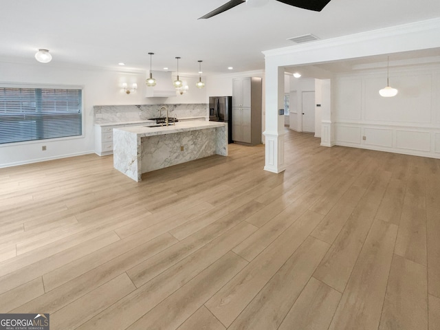 kitchen with decorative light fixtures, white cabinets, a kitchen island with sink, and light stone counters