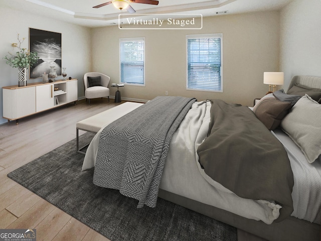 bedroom featuring multiple windows, light hardwood / wood-style flooring, a tray ceiling, and ceiling fan