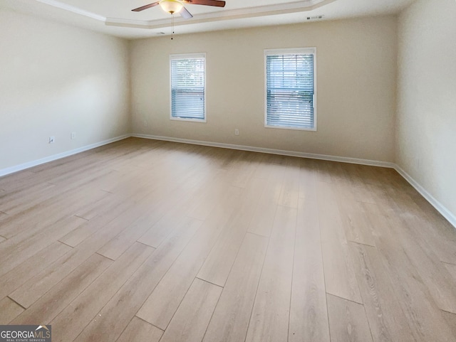 spare room featuring light wood-type flooring, ceiling fan, and a raised ceiling