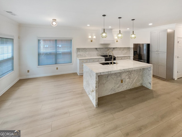 kitchen featuring light stone countertops, a kitchen island with sink, sink, decorative light fixtures, and fridge with ice dispenser