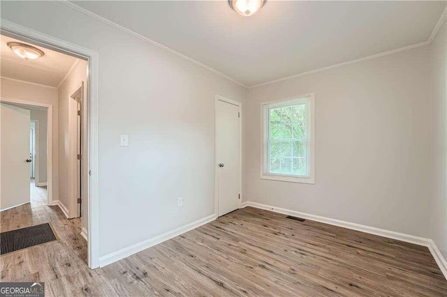 empty room with crown molding and light hardwood / wood-style floors