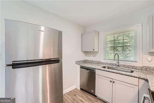 kitchen featuring sink, light stone counters, appliances with stainless steel finishes, light hardwood / wood-style floors, and white cabinets