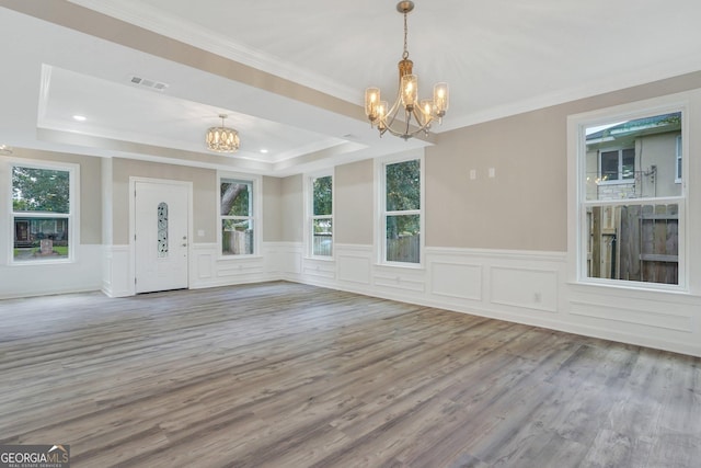 unfurnished dining area featuring ornamental molding, a wealth of natural light, a notable chandelier, and a raised ceiling