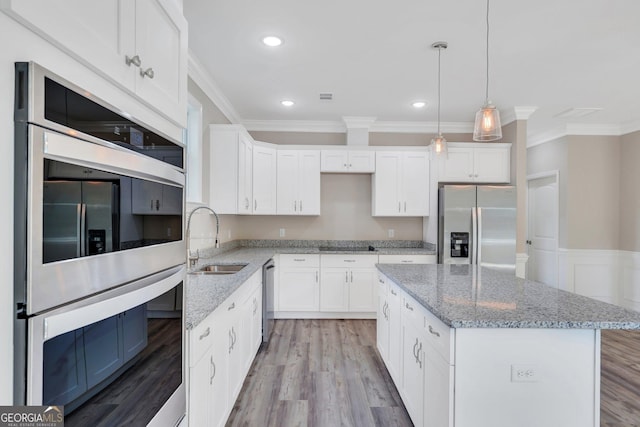 kitchen with pendant lighting, white cabinets, appliances with stainless steel finishes, a kitchen island, and sink