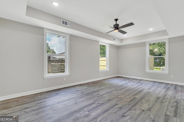 spare room with ceiling fan, a wealth of natural light, a tray ceiling, and hardwood / wood-style floors