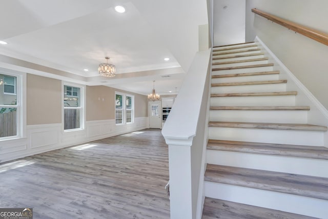 stairs featuring hardwood / wood-style flooring, a raised ceiling, crown molding, and a chandelier