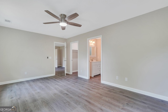 unfurnished bedroom with ensuite bathroom, a spacious closet, sink, light hardwood / wood-style flooring, and ceiling fan