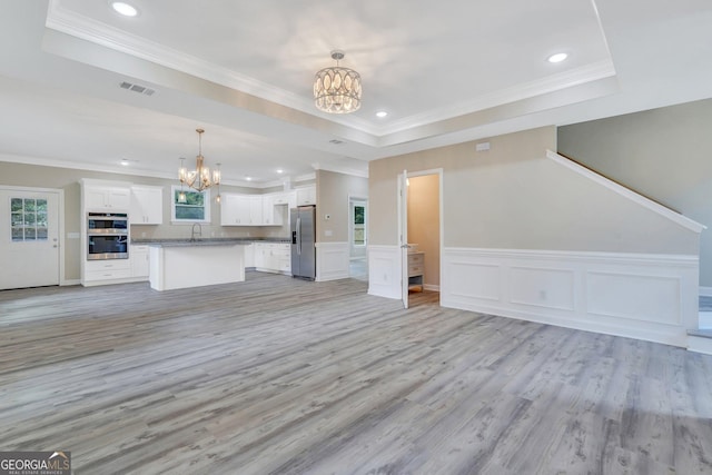 unfurnished living room featuring a raised ceiling, sink, light wood-type flooring, ornamental molding, and a chandelier