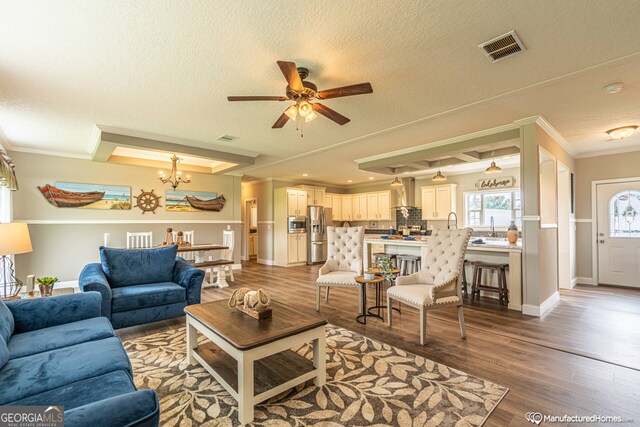 living room featuring a textured ceiling, light hardwood / wood-style flooring, ornamental molding, and ceiling fan with notable chandelier