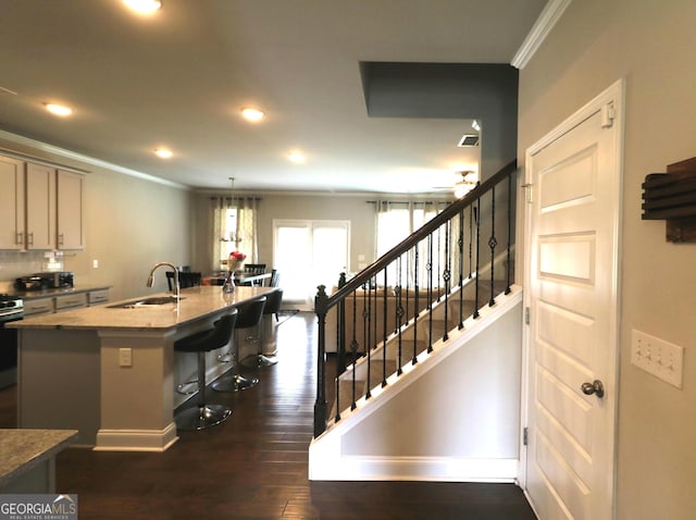 kitchen featuring dark hardwood / wood-style flooring, crown molding, sink, a kitchen breakfast bar, and a kitchen island with sink