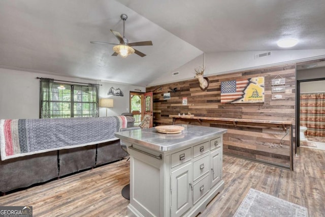 kitchen with light wood-type flooring, a kitchen island, ceiling fan, white cabinetry, and wood walls