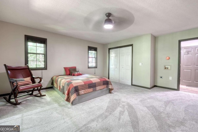 bedroom featuring a textured ceiling, a closet, light colored carpet, and ceiling fan