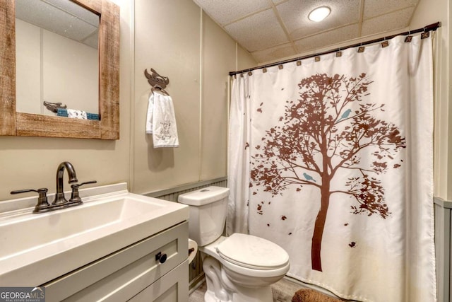 bathroom featuring a drop ceiling, toilet, walk in shower, and vanity