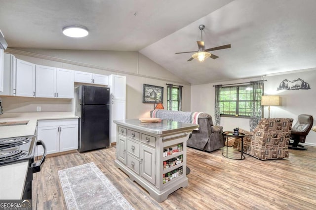 kitchen featuring ceiling fan, light hardwood / wood-style flooring, lofted ceiling, black refrigerator, and white cabinets